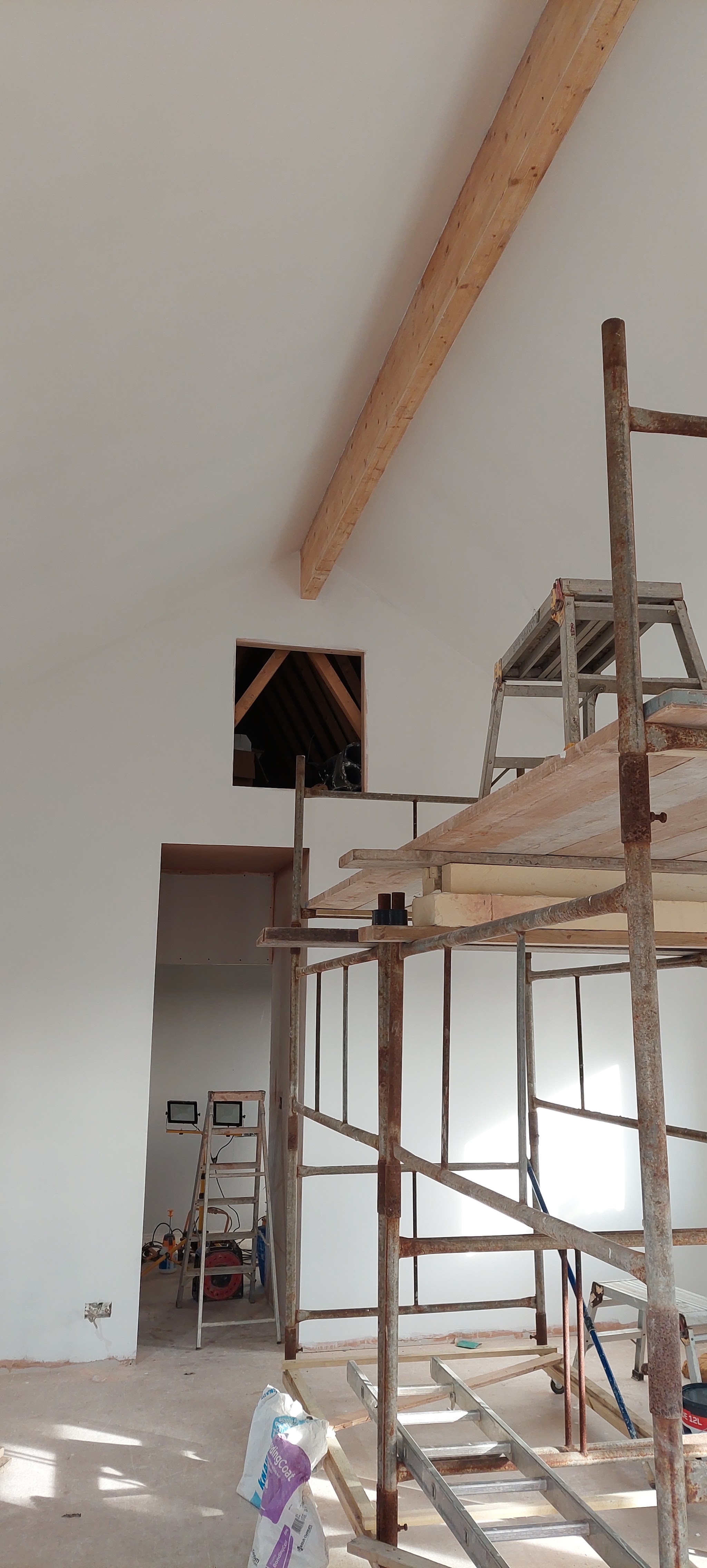 Tall vaulted gable wall with a timber beam, plastered from a scaffold tower