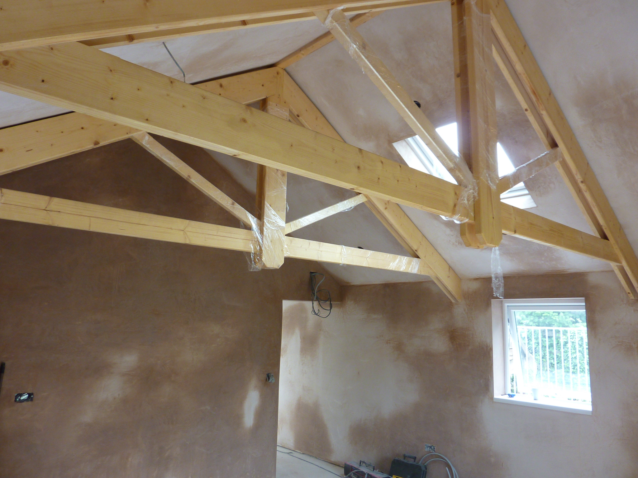 Vaulted room with exposed timber roof trusses and fresh pink plaster drying on the walls