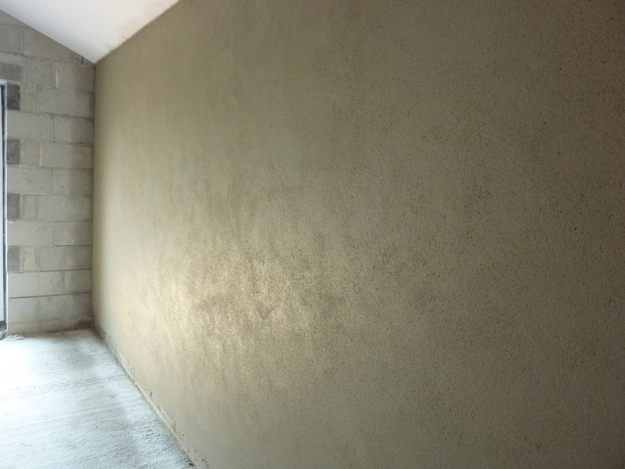 Long wall with a textured sand-coloured plaster finish beside bare blockwork