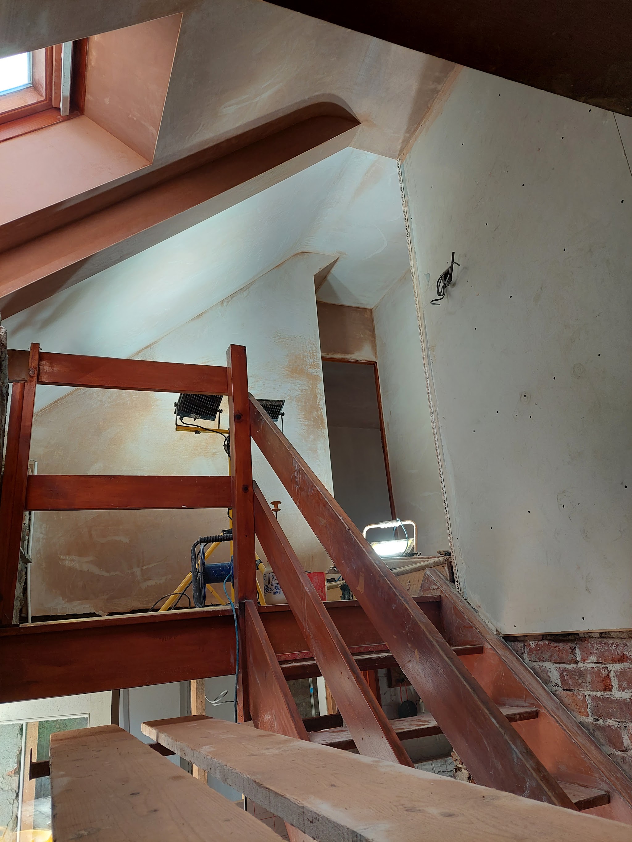 Freshly plastered stairwell walls and sloping ceiling above a timber staircase